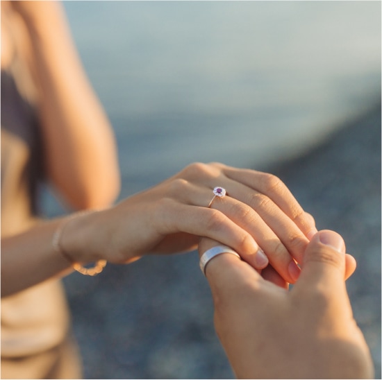 Nahaufnahme einer Person, die einer anderen einen Ring an den Finger steckt, mit einem unscharfen Hintergrund im Freien, der die Romantik eines Hochzeitswochenendes in der malerischen Bodenseeregion einfängt.