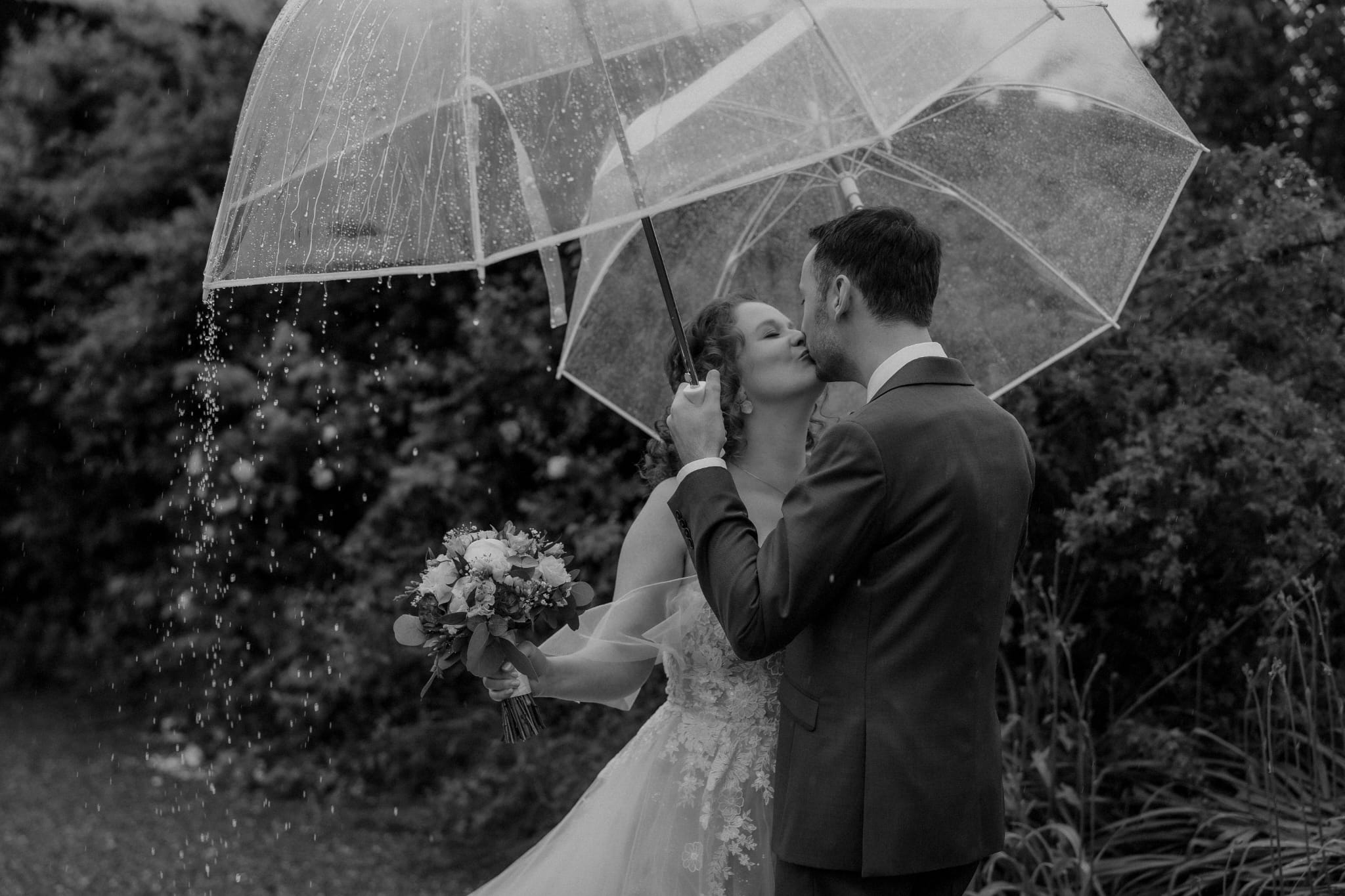 Braut und Bräutigam teilen einen romantischen Moment unter einem Regenschirm an ihrem Hochzeitswochenende in der malerischen Bodensee-Region und schaffen so Erinnerungen für die Ewigkeit.