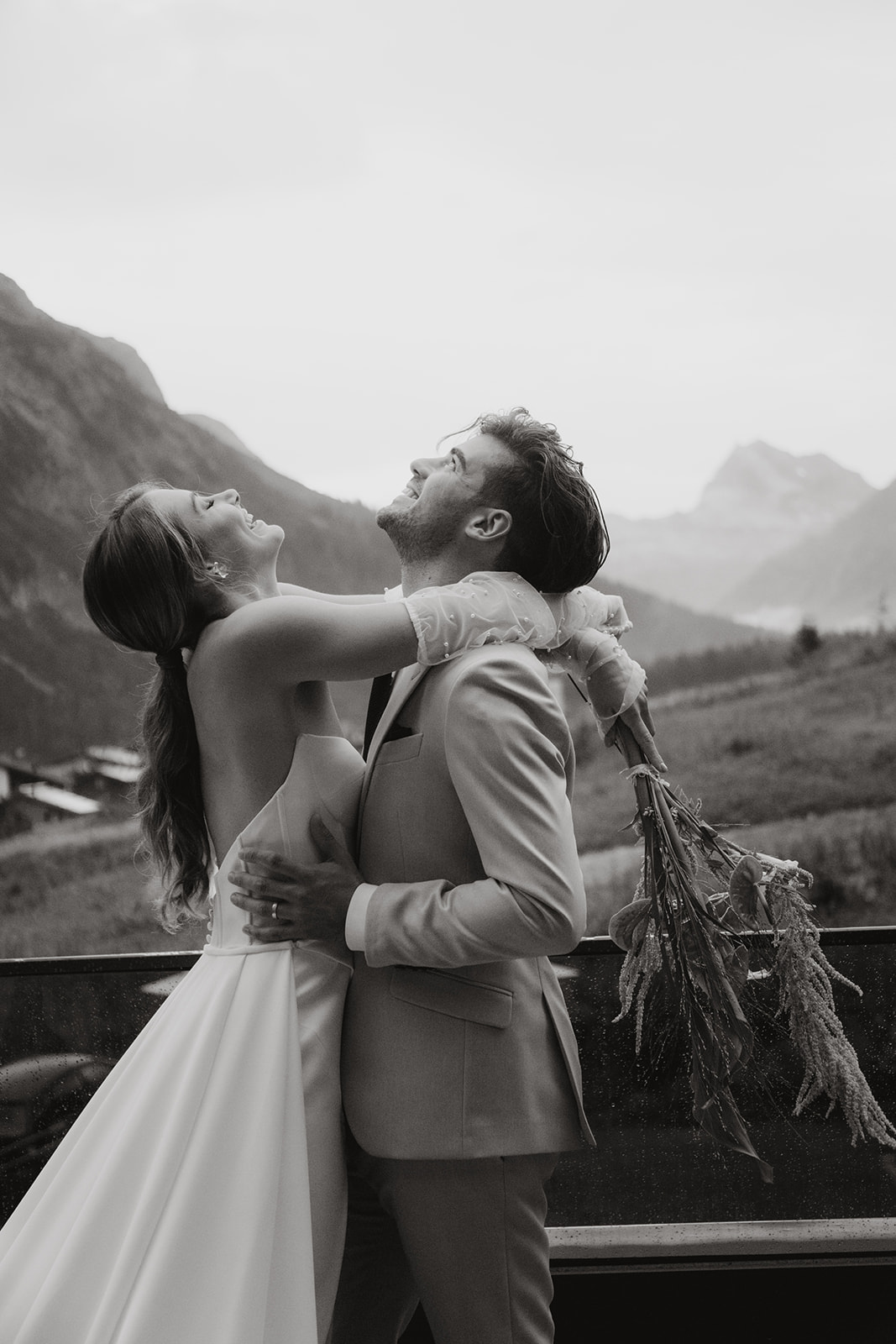 A happy newlywed couple embraces and laughs outdoors, with mountains in the background, celebrating their wedding weekend in South Tyrol.