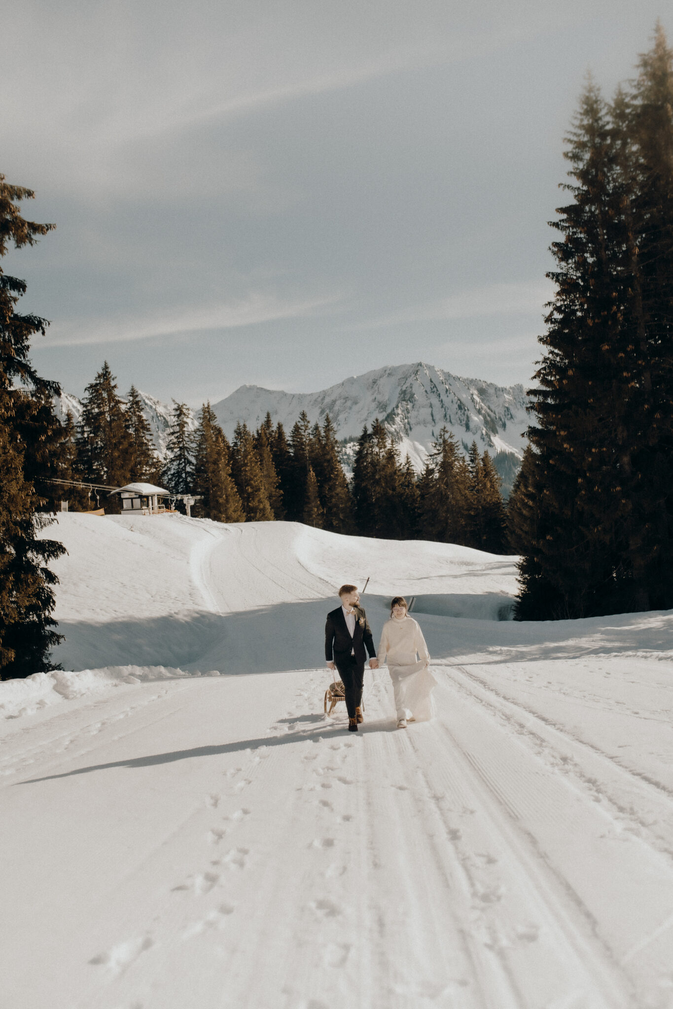 A couple take their dog for a walk in the snow, surrounded by fir trees and mountains under a clear sky, and enjoy a romantic wedding weekend in the picturesque Lake Constance region.