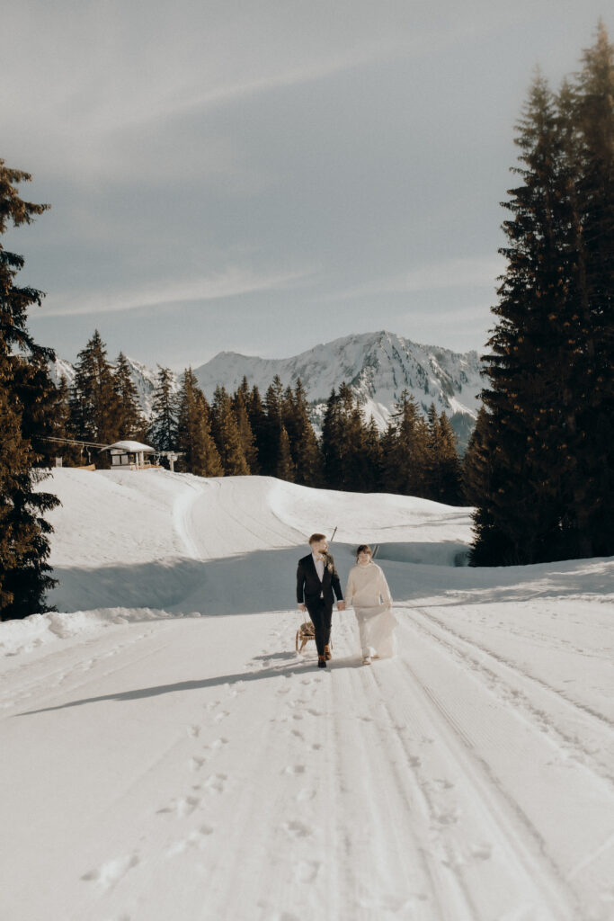 A couple take their dog for a walk in the snow, surrounded by fir trees and mountains under a clear sky, and enjoy a romantic wedding weekend in the picturesque Lake Constance region.