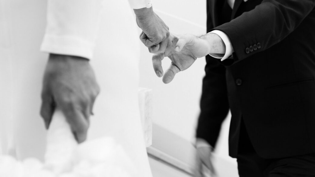 A groom in a suit holds the hand of a bride in a white dress, helping her up the stairs in the scenic Lake Constance region.