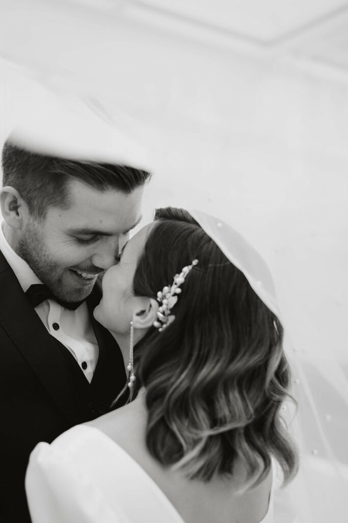 Braut und Bräutigam lächeln sich an ihrem Hochzeitswochenende in der malerischen Bodenseeregion unter einem Schleier zärtlich an.