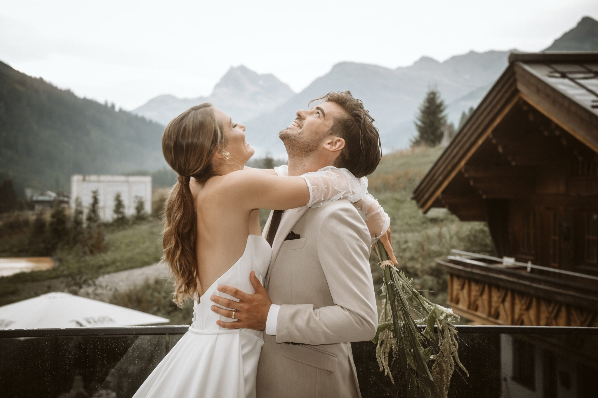 Ein fröhliches Brautpaar umarmt sich und lächelt im Freien, mit den Bergen im Hintergrund, und fängt so die Romantik der Bodensee-Region ein.