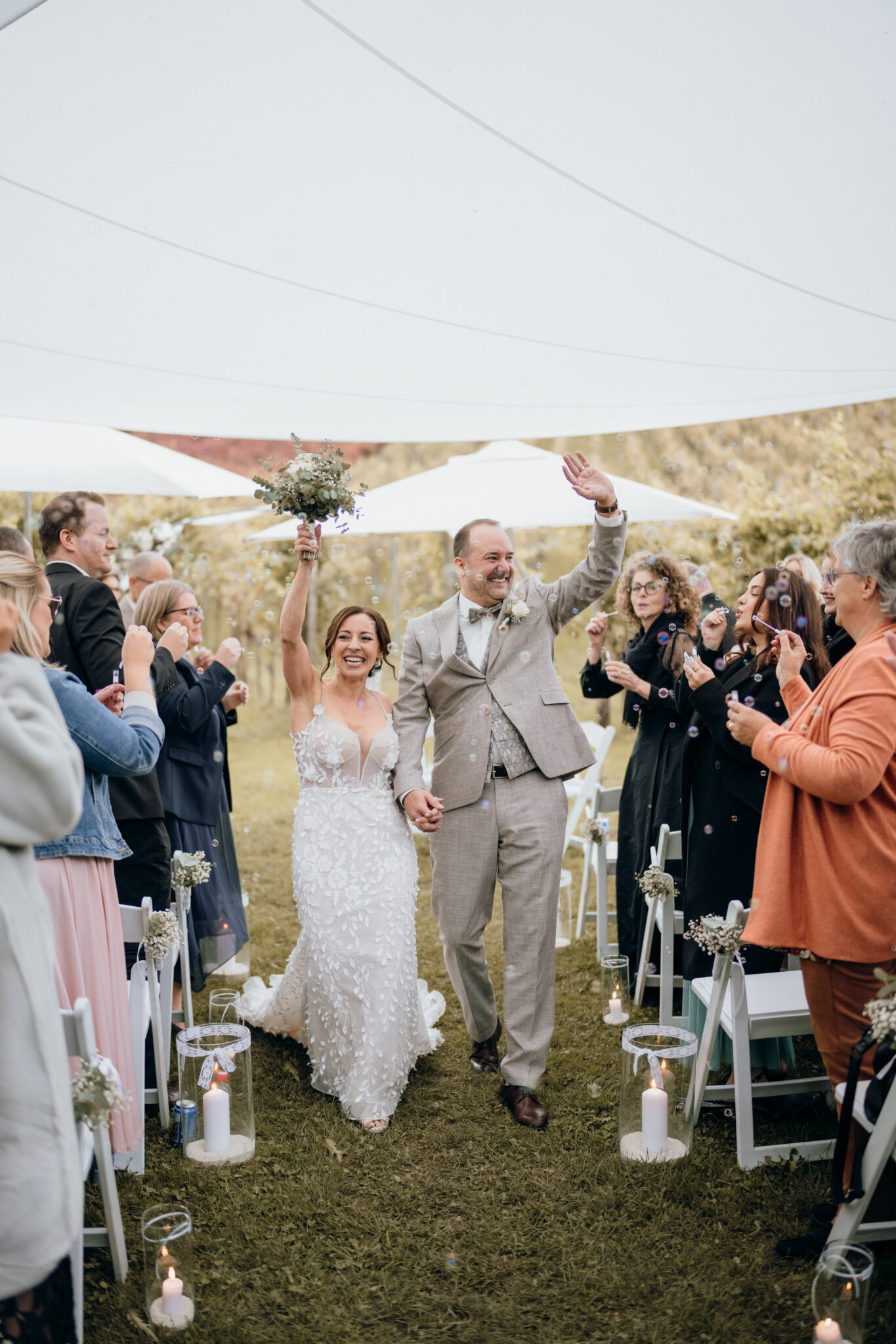 A happy bride and groom walk down the aisle in the picturesque Lake Constance region, hold hands and are cheered on by their guests.