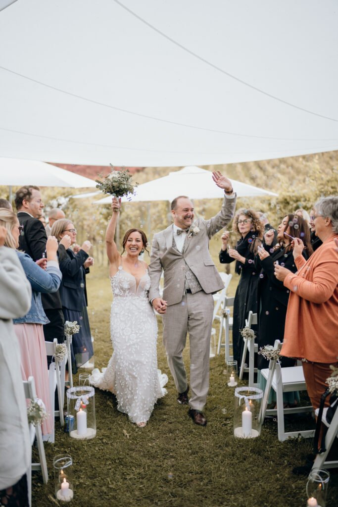 A happy bride and groom walk down the aisle in the picturesque Lake Constance region, hold hands and are cheered on by their guests.