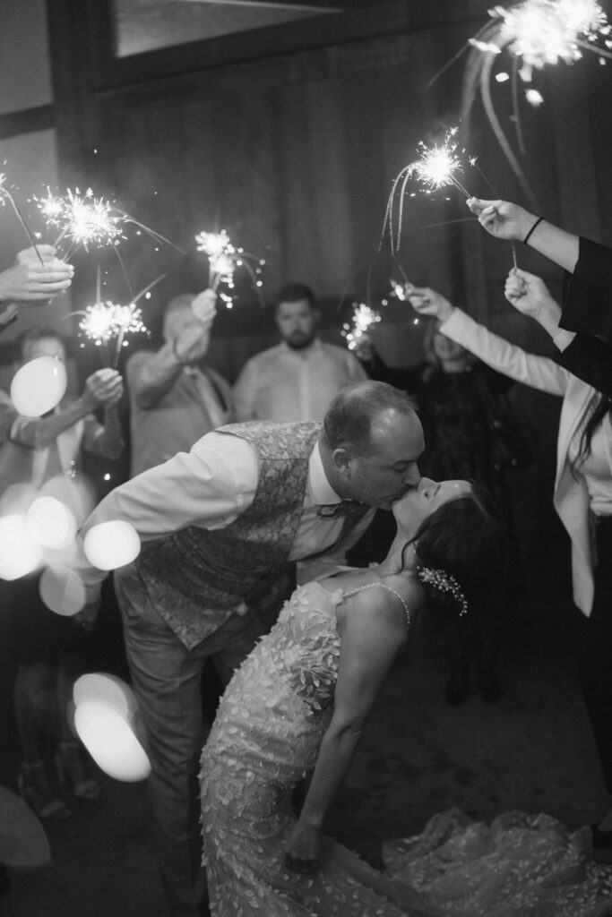 Ein Paar küsst sich, während es von Menschen umgeben ist, die Wunderkerzen in einer festlichen Hochzeitswochenende-Feier halten, und fängt den Zauber der Liebe in Österreich oder der Schweiz ein.