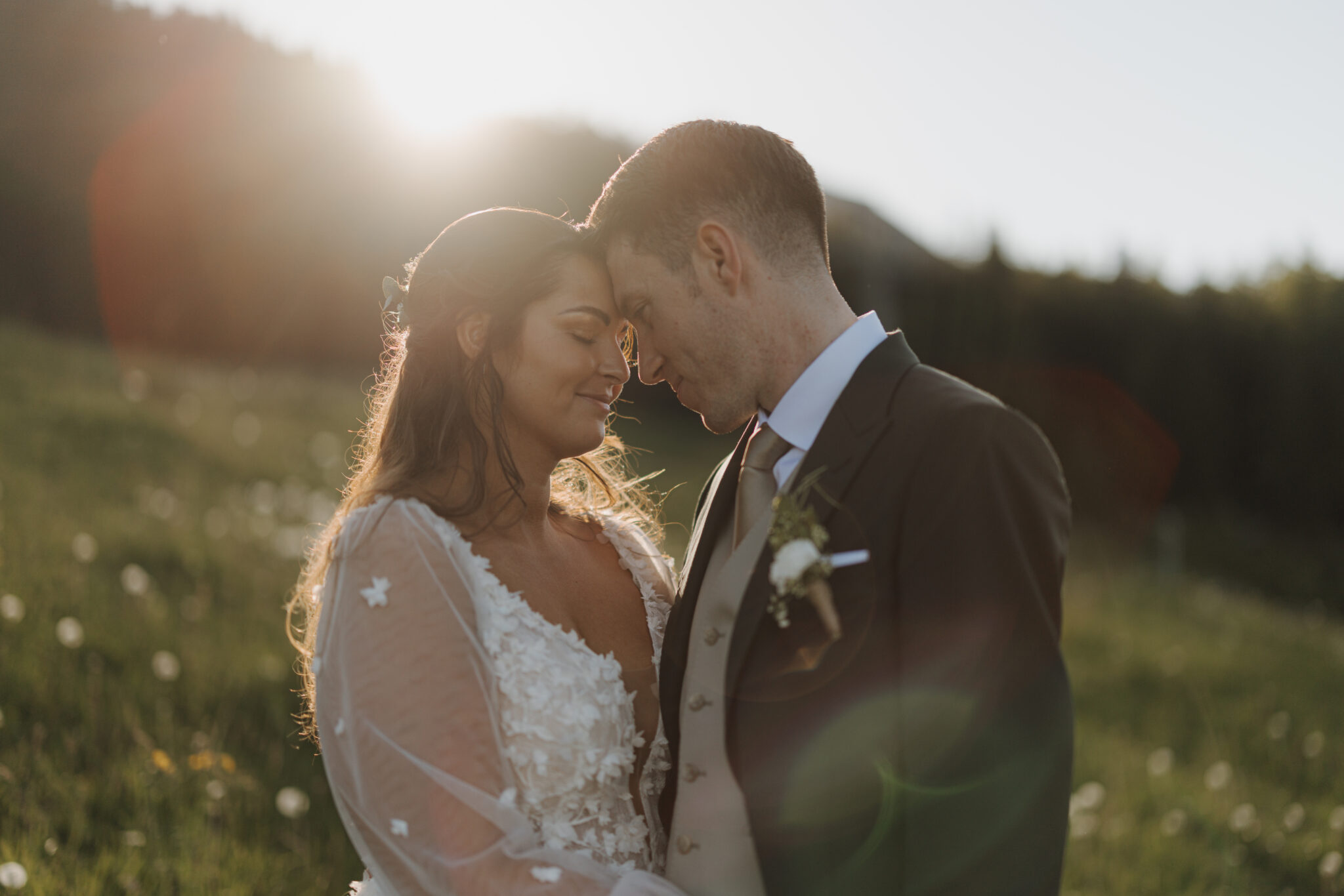 Bride and groom embrace on a sunlit meadow in South Tyrol, touch their foreheads and smile gently at each other on their wedding weekend.