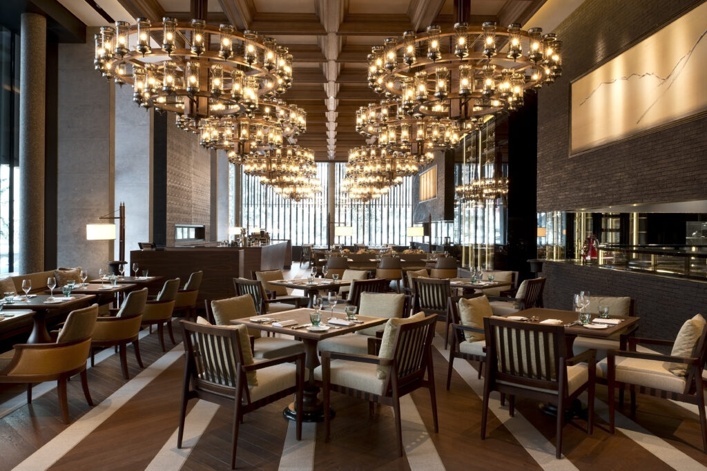 Luxuriöses Restaurantinterieur mit eleganten Kronleuchtern, Holztischen und gepolsterten Stühlen in ordentlicher Anordnung.