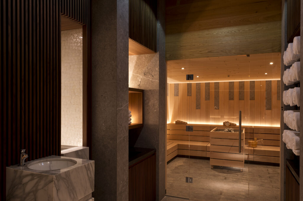 Ein modernes Spa mit einem Marmorwaschbecken, gestapelten Handtüchern und einer Holzsauna mit sanfter, warmer Beleuchtung.